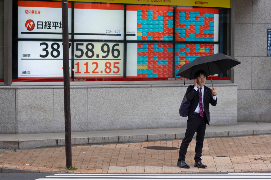 A man stands in front of a live view of the Nikkei 225 index. Photo by Stanislav Kogiku/SOPA Images/LightRocket via Getty Images/Files